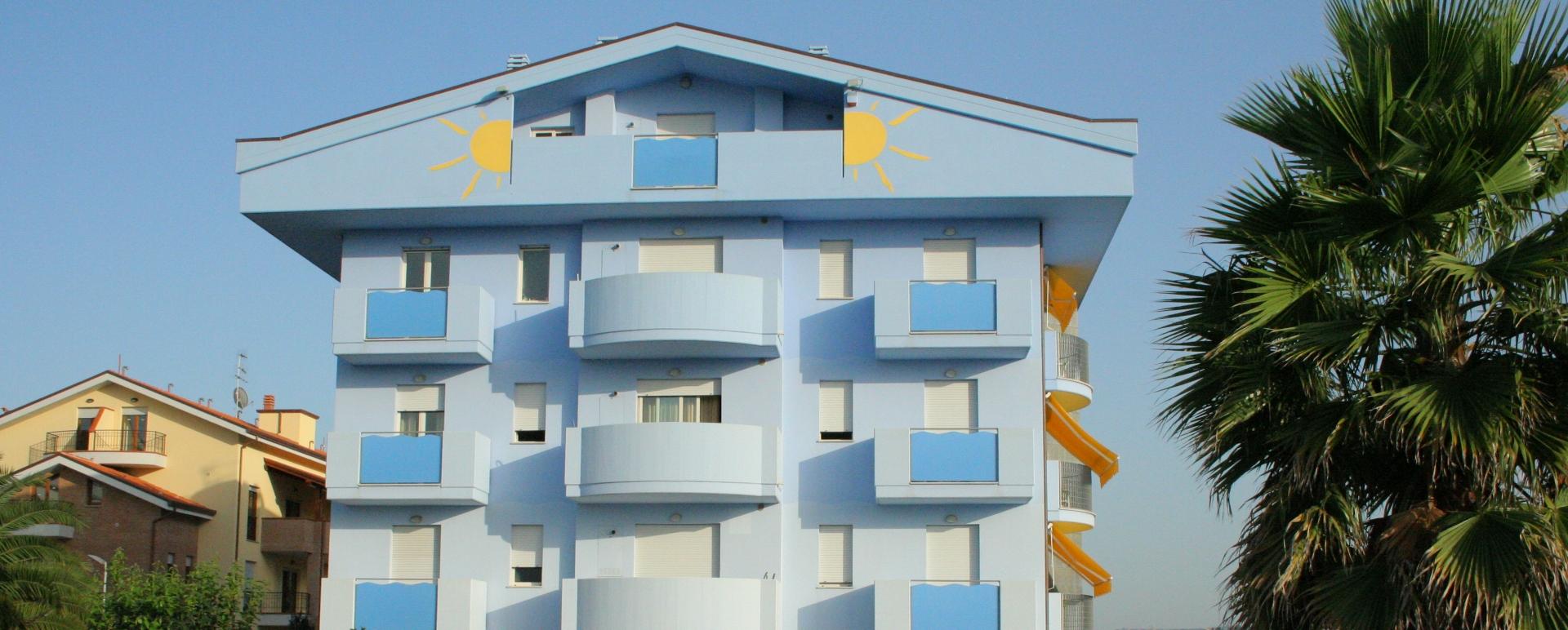 Edificio blu con balconi e disegni di soli gialli sulla facciata.